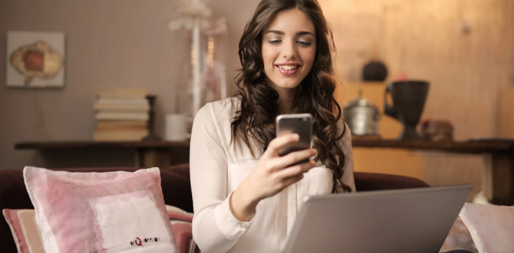 woman sitting on sofa with phone and laptop