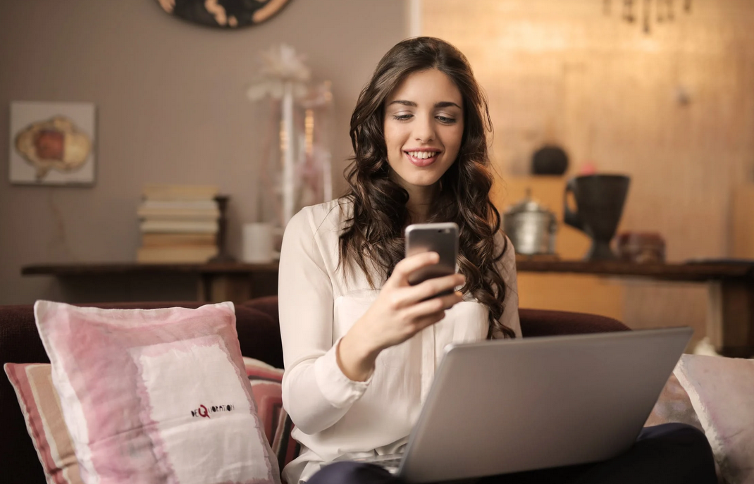 woman sitting on sofa with phone and laptop